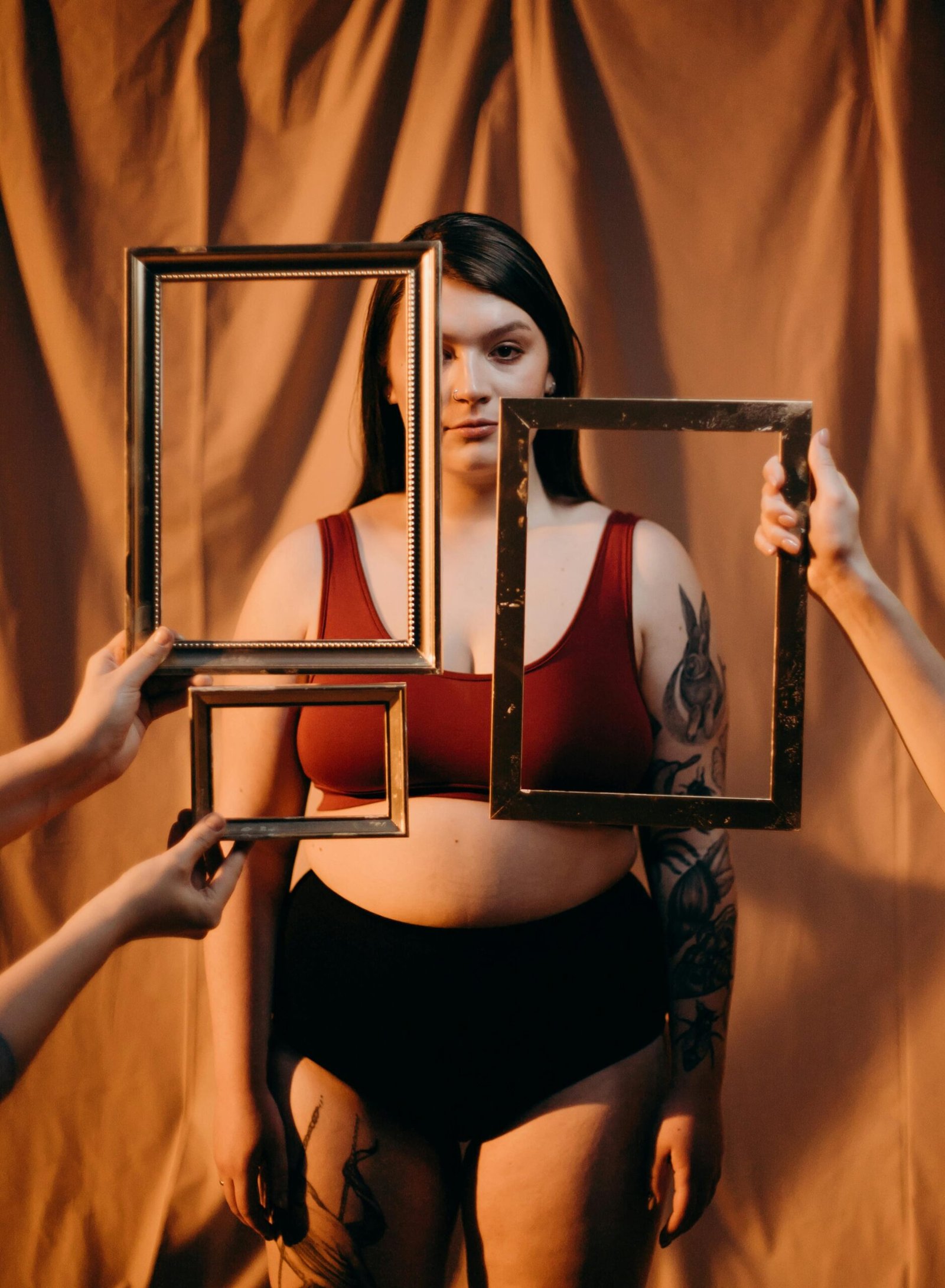 A creative portrait capturing a tattooed plus size woman holding empty frames in a studio setting.